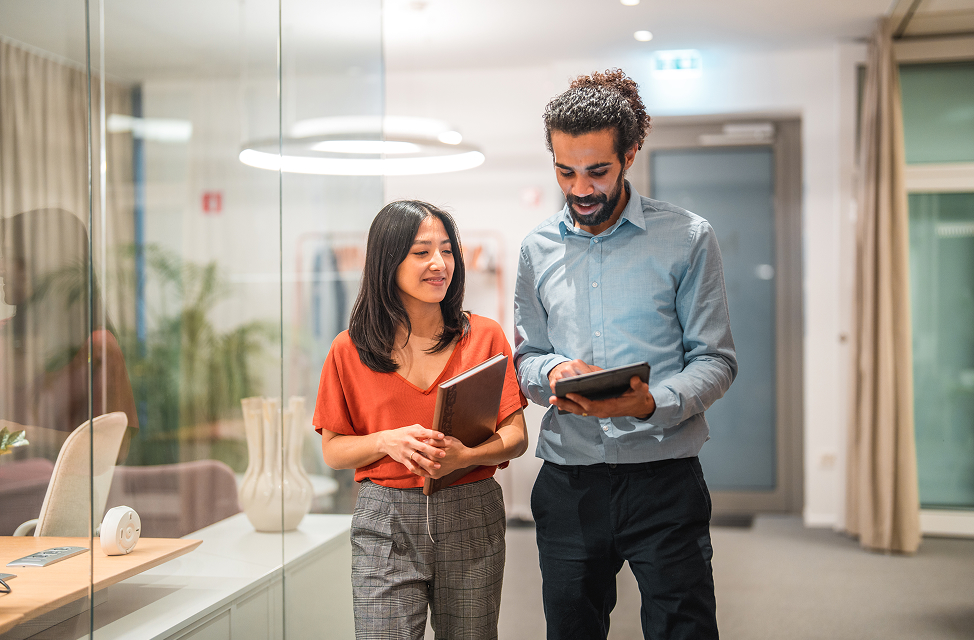 man and women walking down hall discussing benefits on tablet