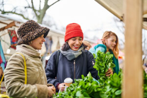 Females wearing warm clothes at vegetable stall in a local market. Women buying vegetables in market on a winter day.