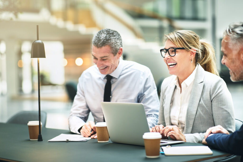 Benefits consultant laughing while having a meeting with two male colleagues at a table in the lobby of a modern office building